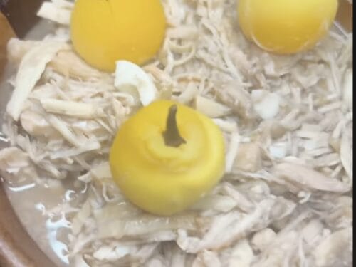 Shredded poultry and white chunks in broth with three yellow whole quinces, one hollowed